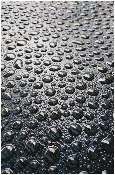 Close-up view of raindrops on a dark textured surf