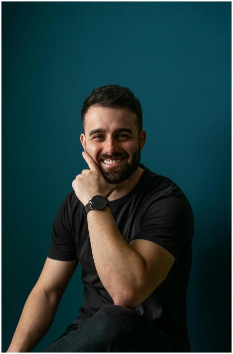 A confident man smiling against a teal background,