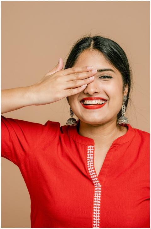 Smiling woman in red top covering one eye, exuding