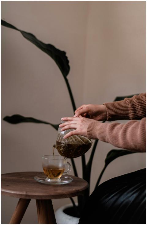 A person pours herbal tea from a glass teapot into