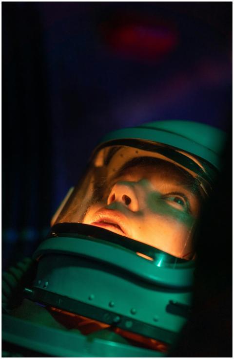 A female astronaut in a space suit looks up, illum