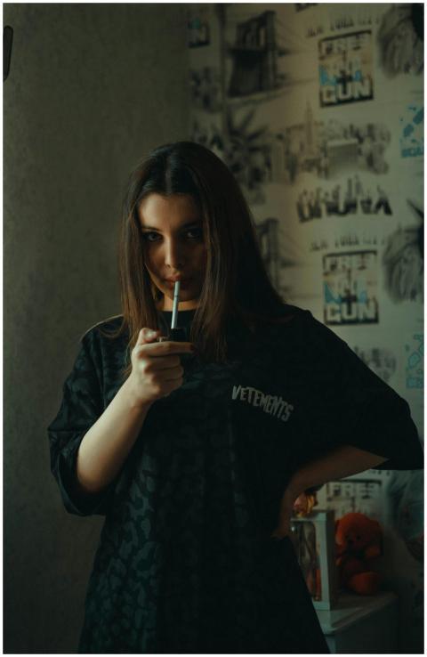 A young woman indoors lighting a cigarette, surrou