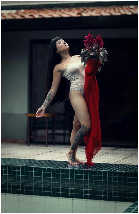 A woman standing by a pool holding flowers, striki