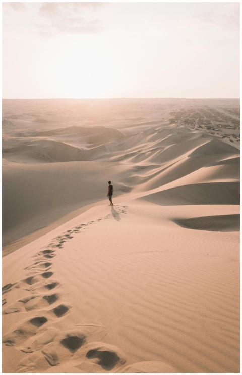 A lone traveler walks across the vast sand dunes o