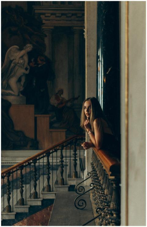 A woman leans on a railing in a museum, gazing con