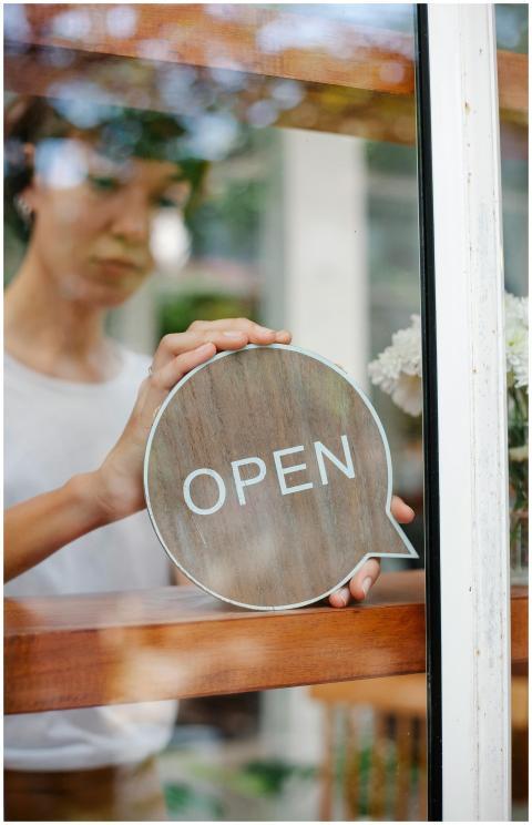 A young woman holding a circular open sign seen th