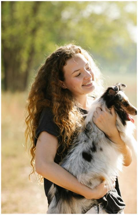 A young woman lovingly holds her happy Shetland Sh