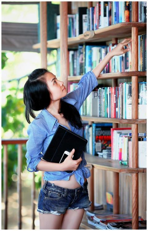 A young woman reaches for a book on a library shel