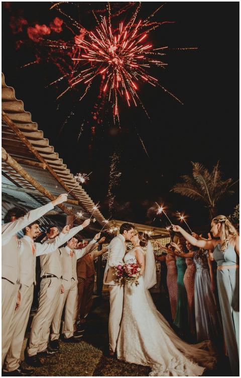 Bride and groom kiss under fireworks surrounded by