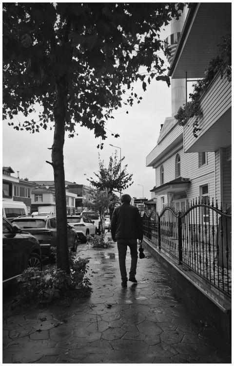 A solitary figure walks down a wet city street lin
