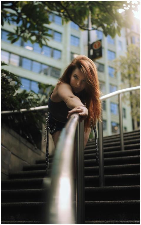 A woman with red hair poses dramatically on a city