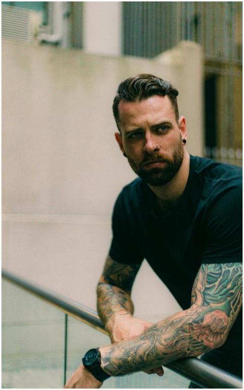 Portrait of a stylish, tattooed man leaning on a r