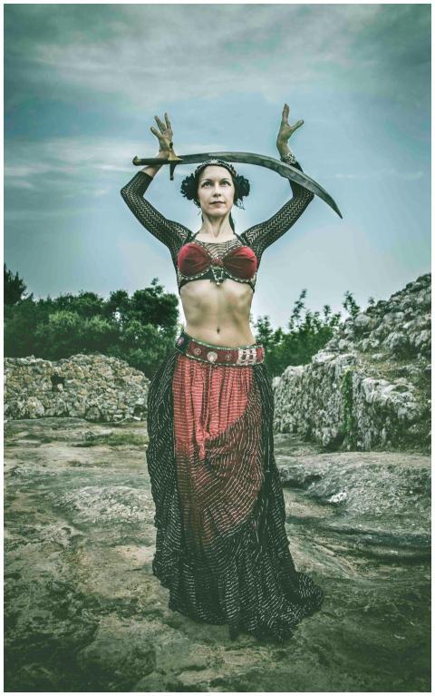 A woman in a tribal costume holds a sword overhead