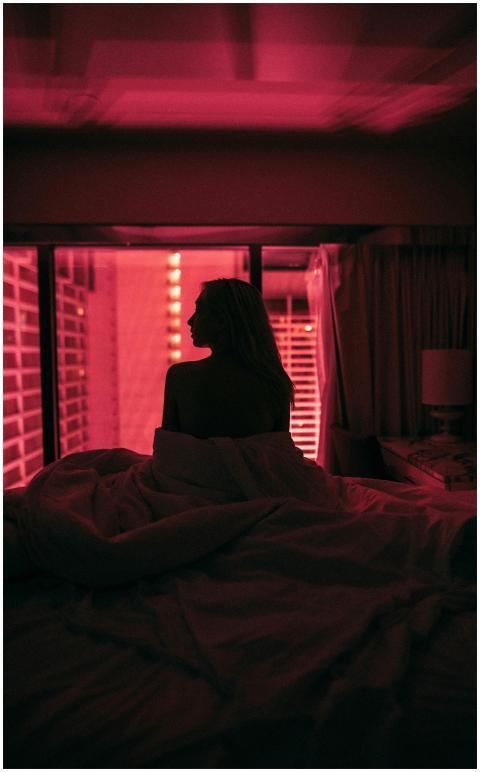 A woman sitting on a bed in a dark room illuminate