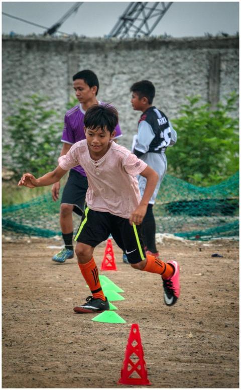 Ethnic kid running through training cones while pl