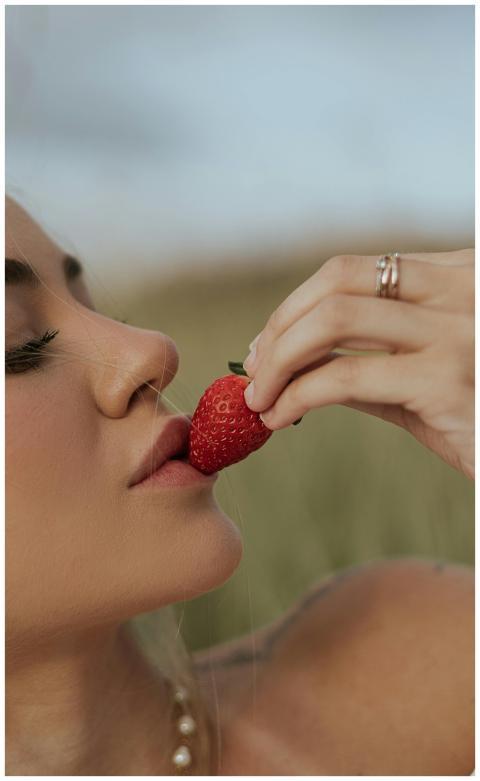 Close-up of a woman gently biting into a fresh str