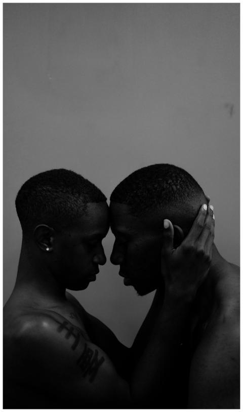 Two shirtless men share a tender moment, embodying