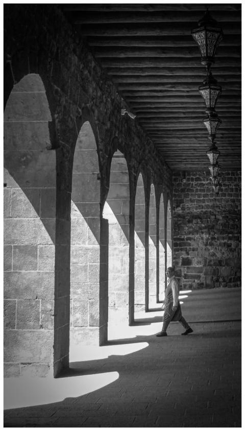 A person walks through a sunlit stone corridor wit