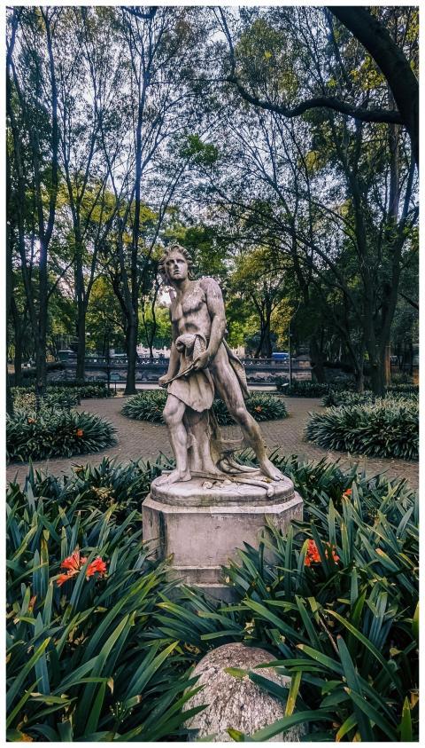 Marble statue in a vibrant city park surrounded by