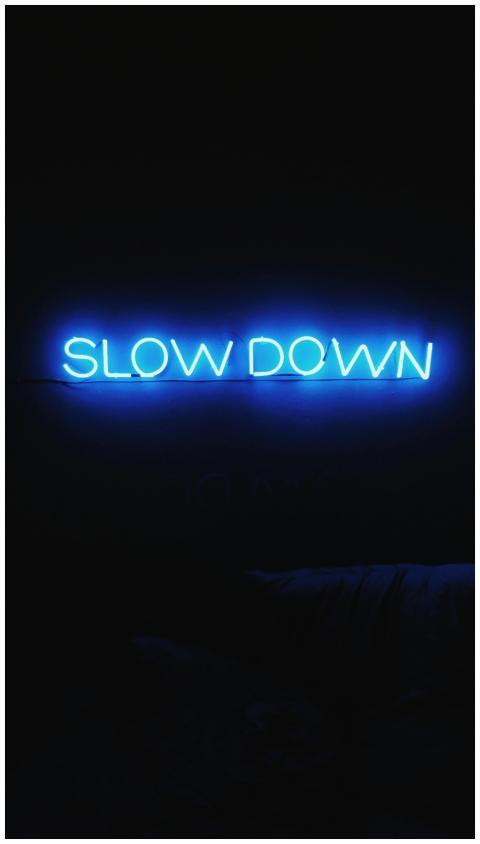 A glowing blue neon sign reads 'Slow Down' against