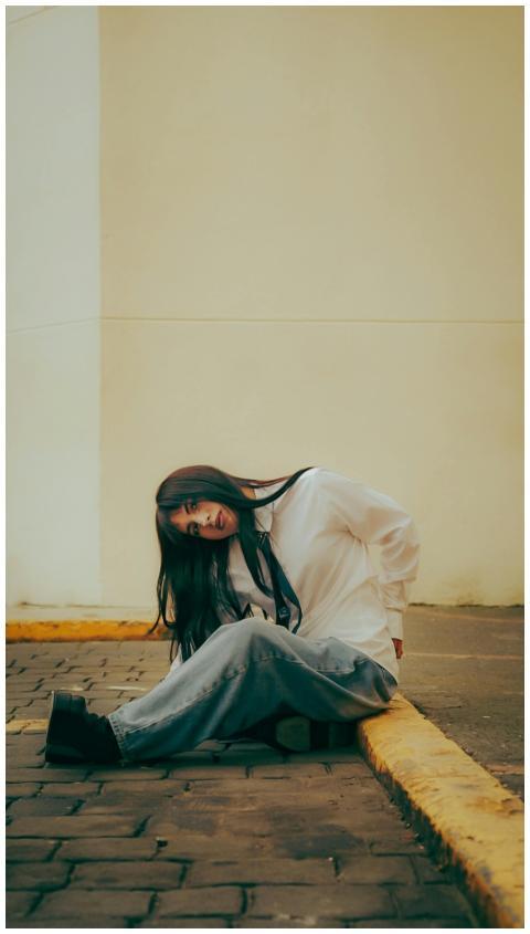 A young woman in casual clothing sits on a street