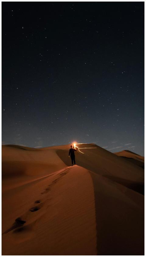 A lone figure walks across desert dunes beneath a