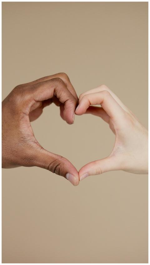 Two hands of different ethnicities form a heart sh