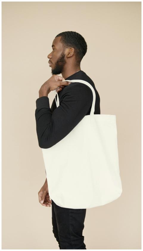 Profile of a young man holding a white tote bag, s