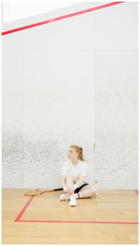 A woman in sportswear sits on a squash court floor