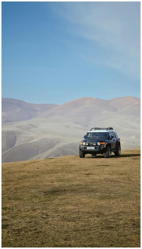 A lone SUV parked on a grassy hill with distant ba