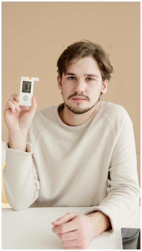A young man showing a blood glucose meter, focusin