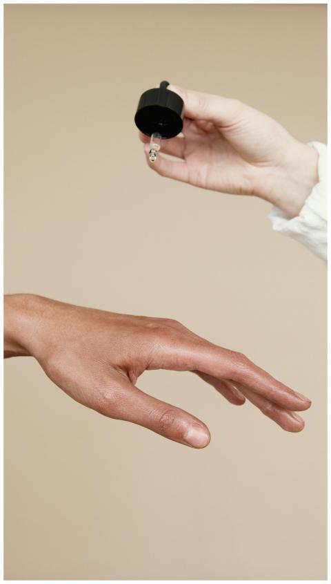 Two hands applying skin care oil with a dropper. I