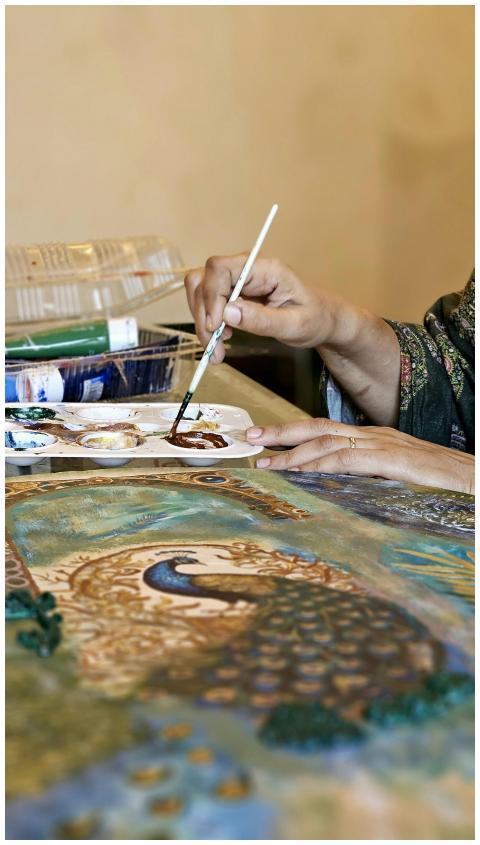 Close-up of hands painting a peacock with detailed