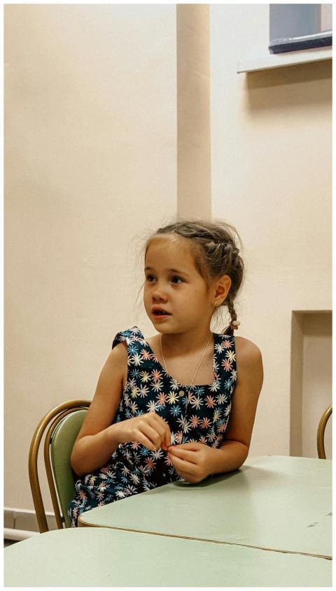 A young girl seated indoors, looking attentive in