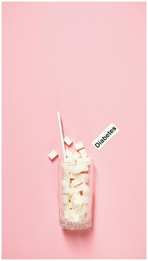 Glass of sugar cubes and diabetes label on pink ba