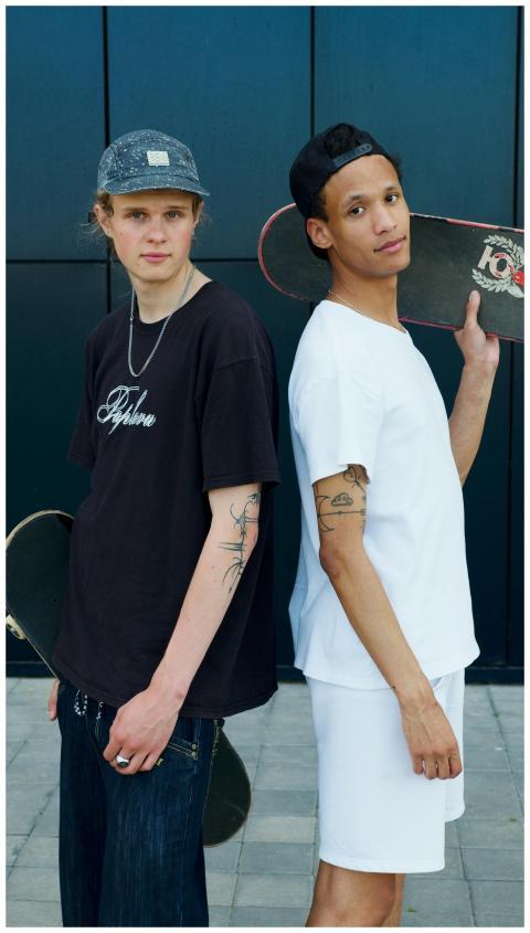 Two young men posing with skateboards outdoors aga