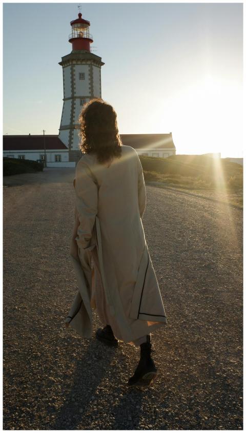 A person in a coat walks towards a lighthouse duri