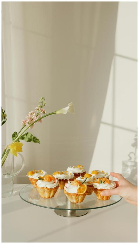 A glass tray of cupcakes with cream and citrus, pe