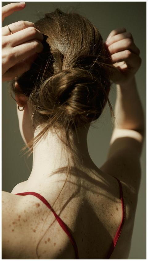 A woman adjusting her hair in a bun, casting shado