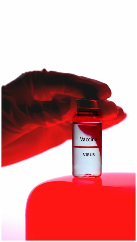 A close-up of a vaccine vial held by a gloved hand