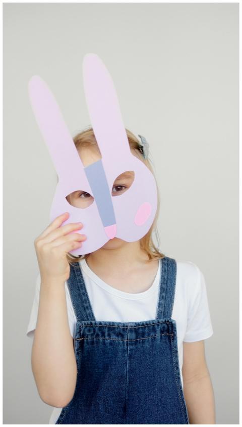 Young girl holding a colorful bunny mask in an ind