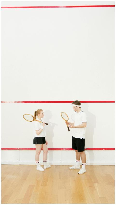 A young man and woman practice squash on an indoor
