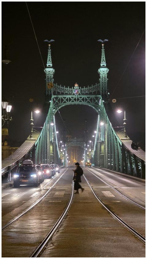 A woman crosses the illuminated Liberty Bridge in