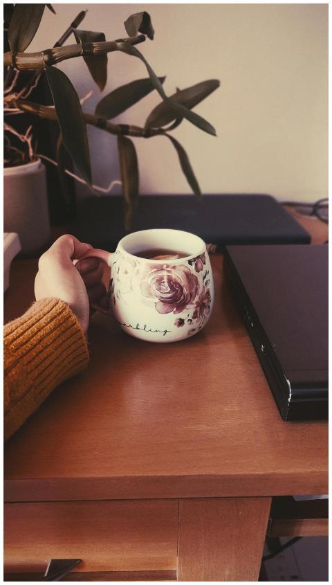 A comforting cup of tea held near a laptop in a co