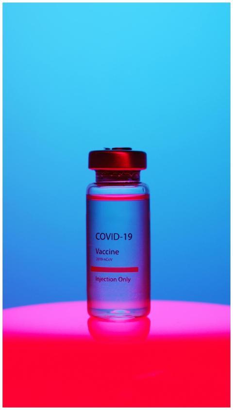 A COVID-19 vaccine vial on a vibrant blue and red
