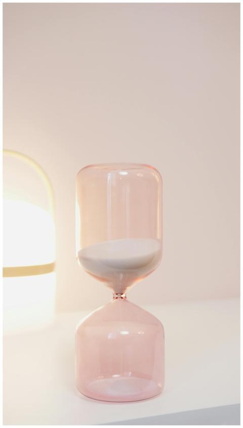 Elegant pink hourglass on a white shelf with soft