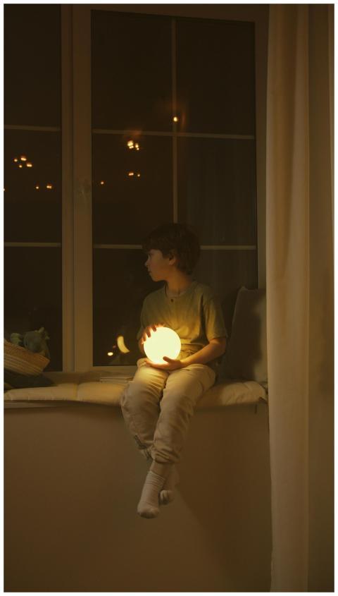 A child holding a glowing orb, sitting on a window