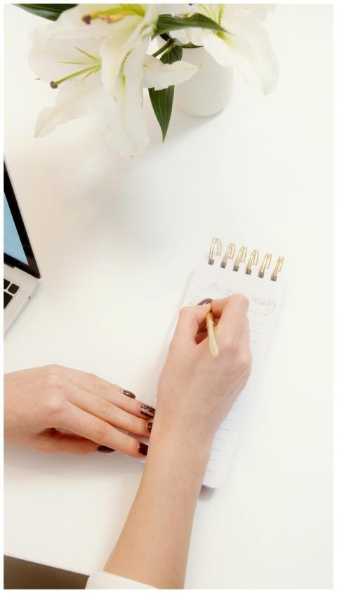 Female hand writing in notepad on a clean desk wit