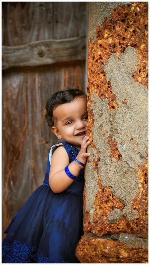 A delightful baby girl in a blue dress peeking aro
