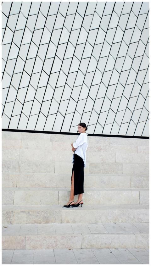 Woman in black skirt and white shirt poses on mode
